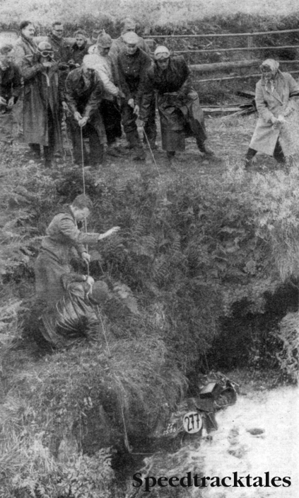 Photo - In the Drink: rescue team retrieves the 500cc Velocette of Dutch Rider Theobald Witberg after its twenty-feet plunge from a wooden footbridge into a mountain stream near St. Anna. Witberg held onto the vegetation and kept dry.