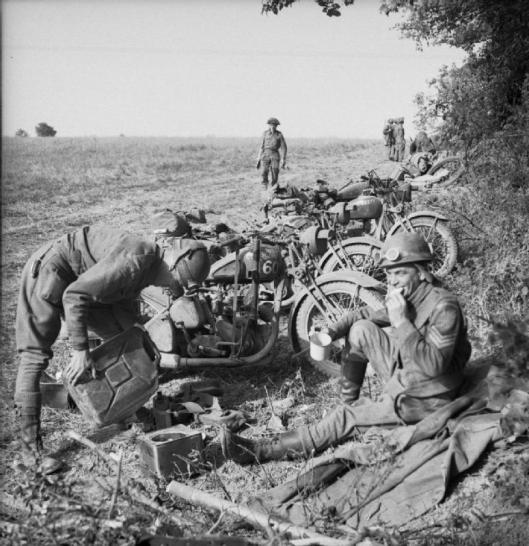 Photo - Sgt J Lloyd (right) and L/Cpl Jones, two motorcycle despatch riders of the Royal Welsh Fusiliers have a 'brew' before the attack on Evrecy, 16 July 1944. (Image courtesy Imperial War Museum)