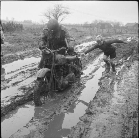 Photo - A small boy helps a motorcycle despatch rider negotiate a muddy road in Holland, 11 December 1944. (Image courtesy Imperial War Museum)