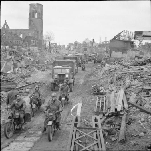Photo - Trucks and motorcycles pass through Stadtlohn, 1 April 1945. (Image courtesy Imperial War Museum)
